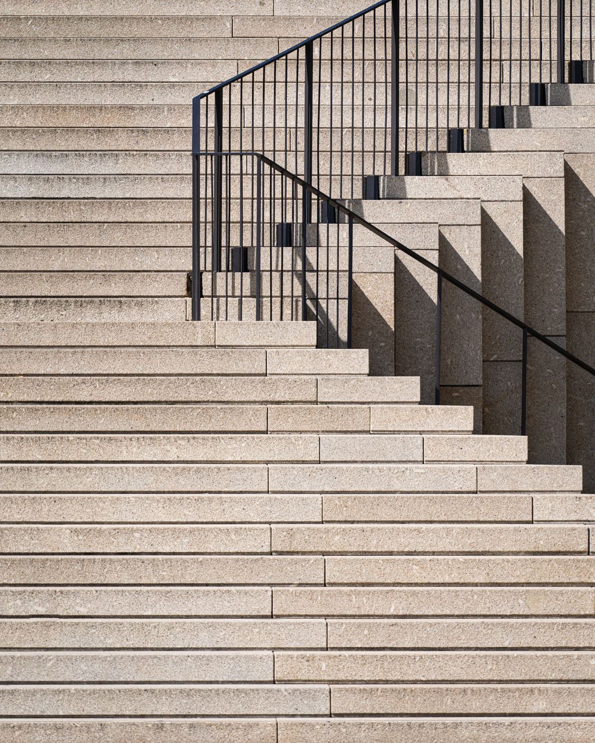 Pale stone staircase with a slim black handrail in soft daylight